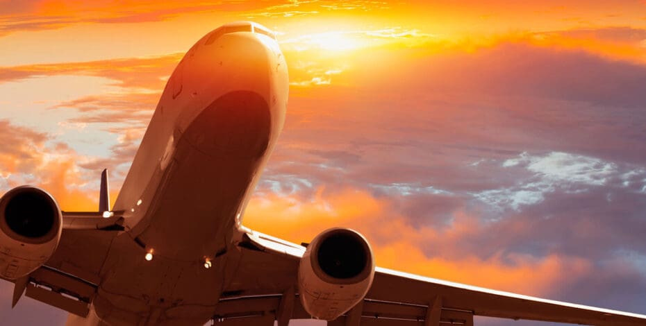 Airplane flying above tropical sea at sunset