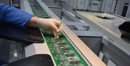 A person wearing a glove is carefully placing components on a single-sided printed board circuit.