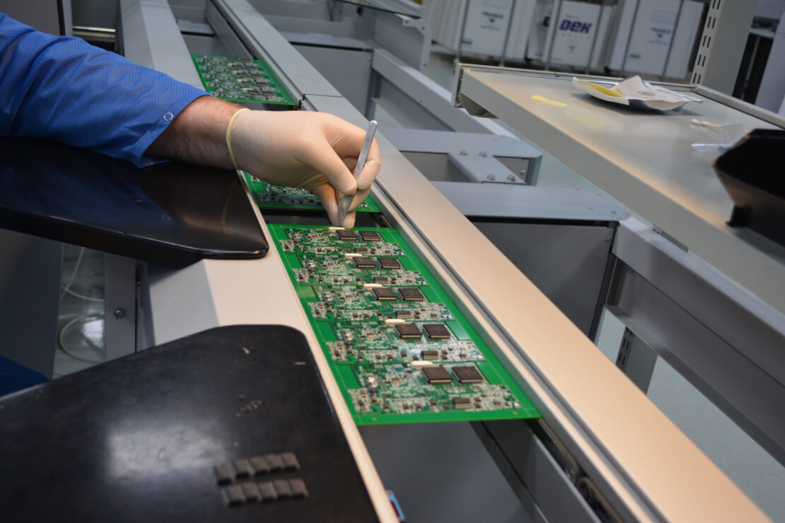 A person wearing a glove is carefully placing components on a single-sided printed board circuit. 