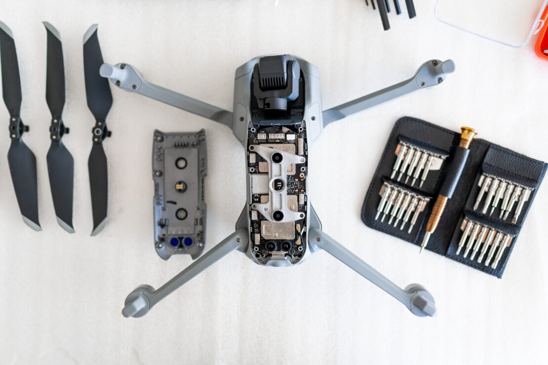 A top view of a disassembled drone/quadcopter. Next to the disassembled drones are three prop blades and a wallet of assembly tools.